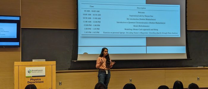 Shohini standing in front of the students with her presentations slides projected behind her on a big screen.